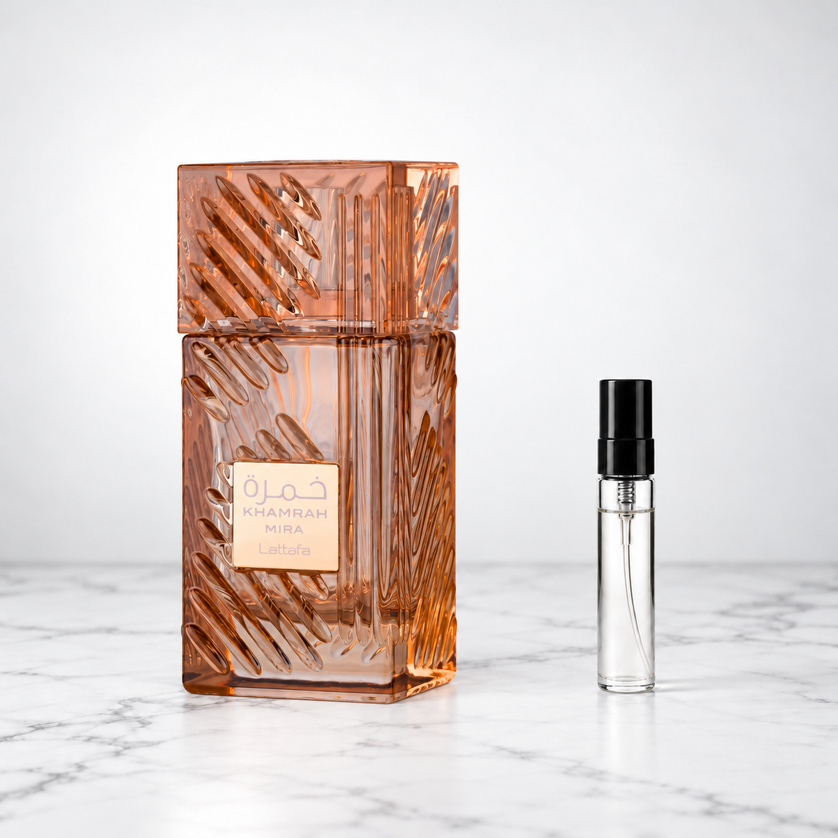 Khamrah Mira by Lattafa perfume bottle beside a sample decant on white marble